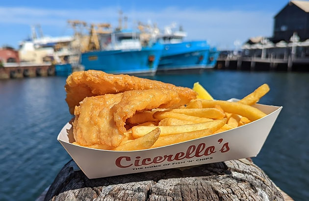 A close up of a box of fish and chips with blue fishing boats in the background