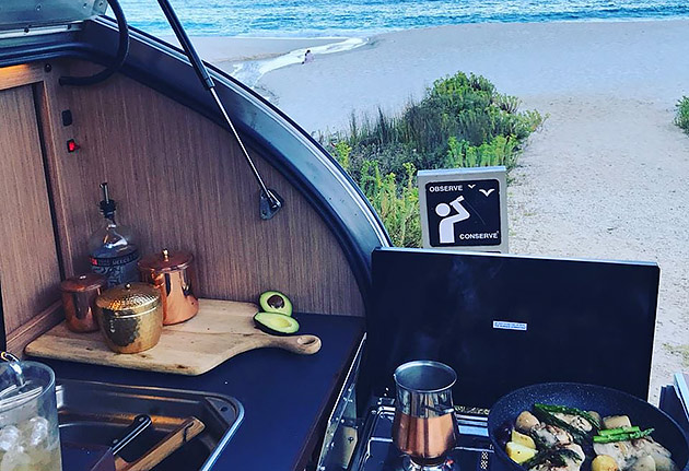 The modular kitchen in the rear of a teardrop camper parked at the beach