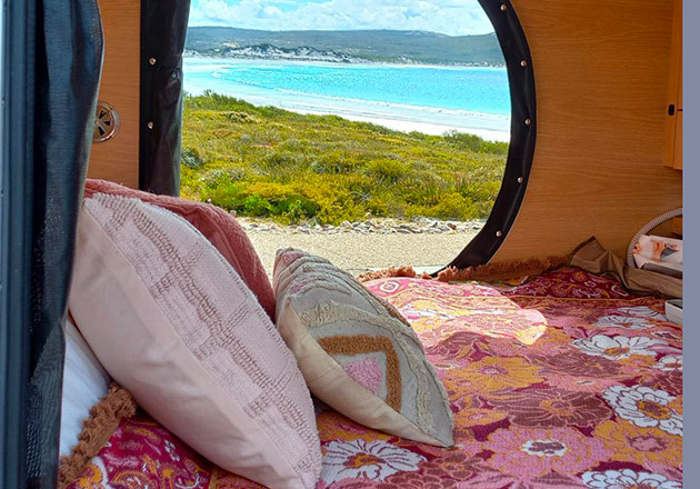 The interor of a teardrop camper with a curved window showing a beach view