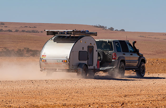 A teardrop camper being towed on a gravel road