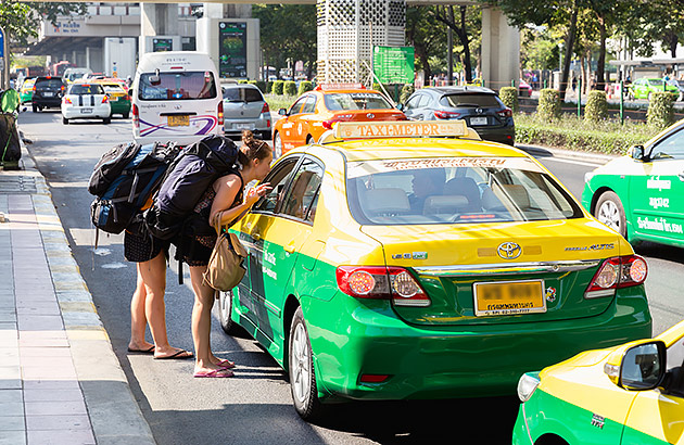 A row of taxis in Thailand with a backpacker leaning into the window of one