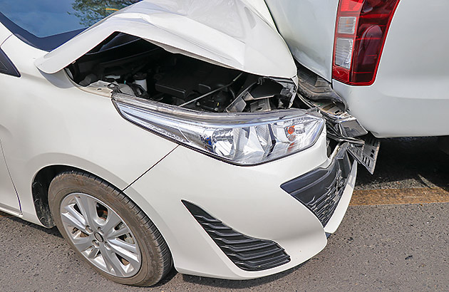 A small white car has crashed into the bumper of a large car