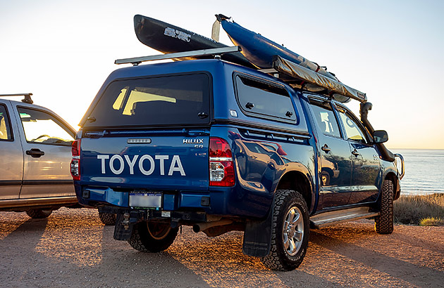 A Blue Toyota Hilux with kayaks on the roof parked at the beach