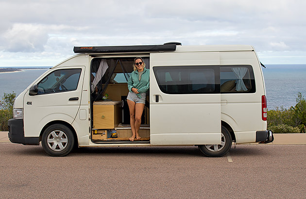 A woman standing in the doorway of a campervan at the beach