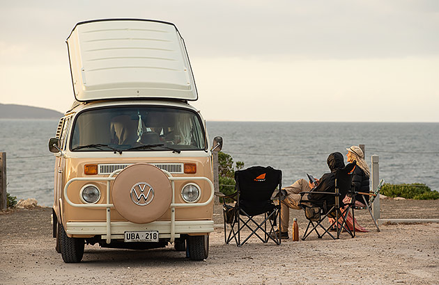 Two people sitting near a VW Kombi van by the beach