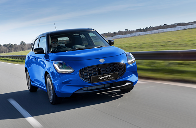 A blue 2024 Suzuki Swift driving down a road