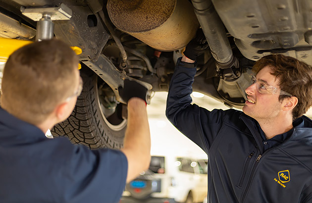 Two car mechanics working beneath a car on a hoist