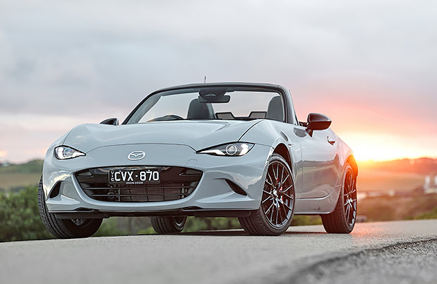 A white Mazda MX-5 GT on a country road at sunset