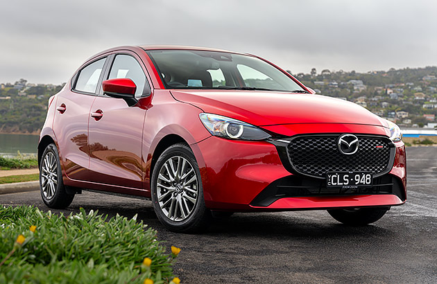 A red Mazda2 parked near a lake