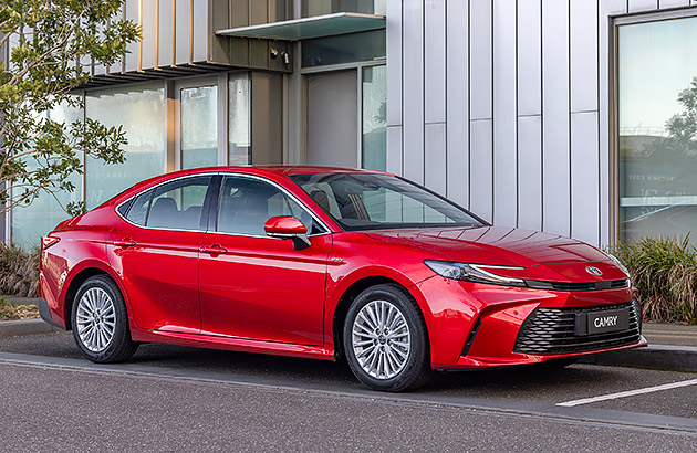 A red Toyota Camry parked in front of a modern building