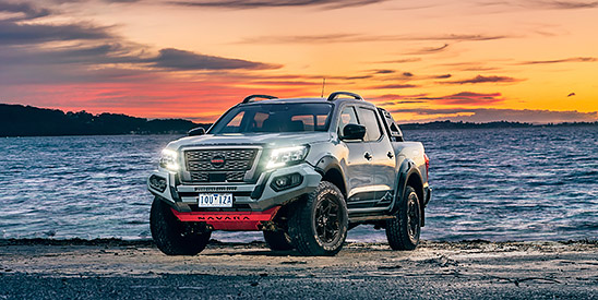 A black Nissan Navara parked on a beach at sunset