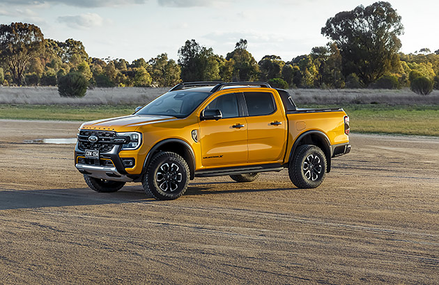 A yellow Ford Ranger Wildtrax parked on sandy ground in a country setting