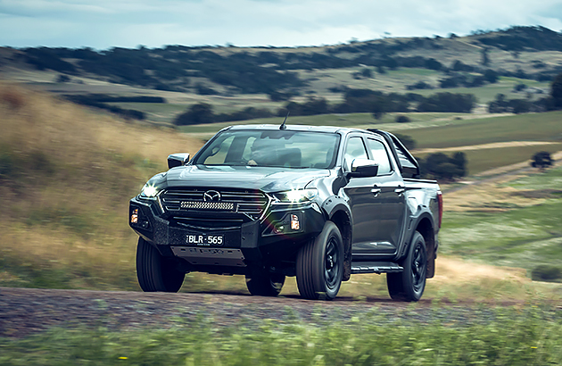 A dark grey Mazda BT-50 Thunder driving up a track on farmland