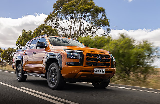 An orange Mitsubishi Triton driving on a country road