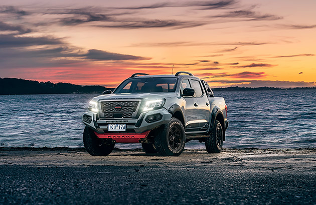 A black Nissan Navara parked on a beach at sunset