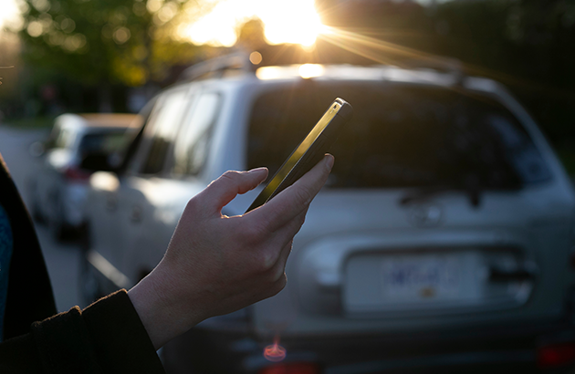 Phone being used on sidewalk by parked cars