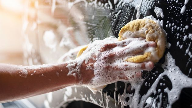 Person hand washing car with yellow sponge and soap