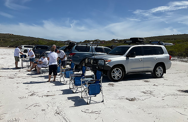 A row of four-wheel drives and their owners on a beach