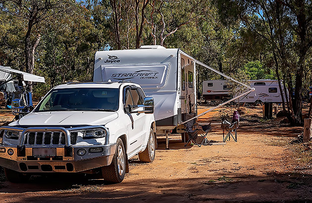 A caravan park with a caravan set up with its awning out in the mid-ground