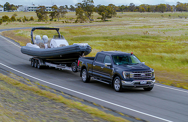 A black Ford F-150 towing a boat on a country road