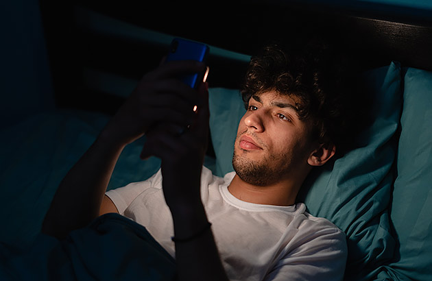 A young man in bed looking at his mobile phone