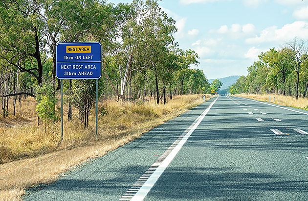 A country road showing a rest stop sign