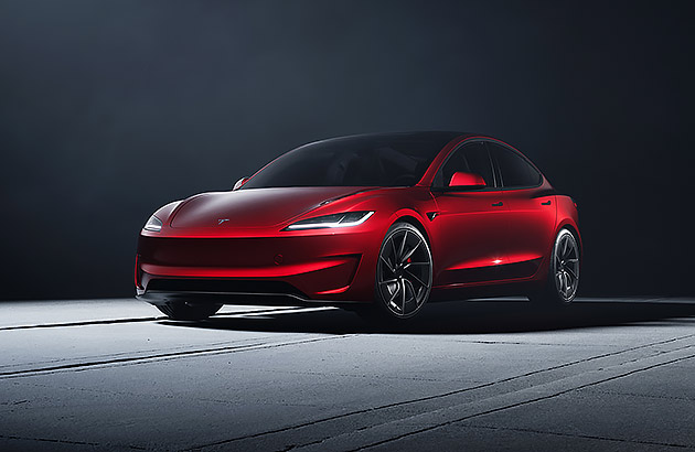 A red Tesla Model 3 under a spotlight in a dark studio