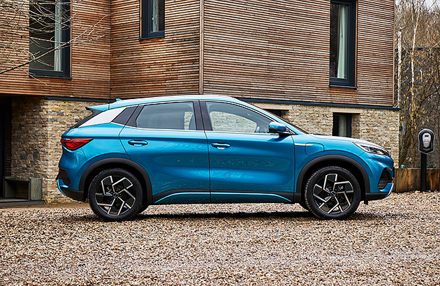 A blue BYD Atto 3 parked in front of a brick wall