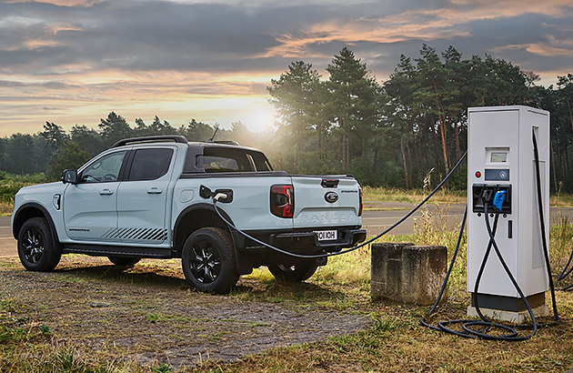 A white Ford Ranger EV parked at a charger in a country landscape