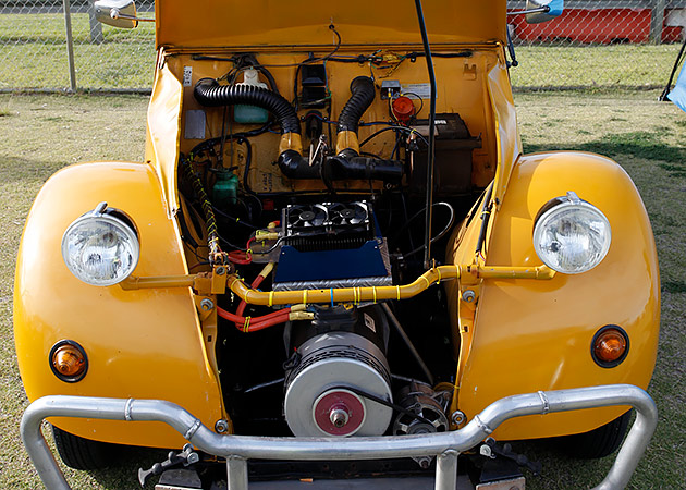 A yellow-coloured classic car with its bonnet up showing an EV battery pack
