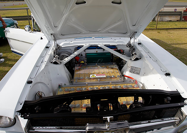 A white Ford Mustang with its bonnet up showing a large battery pack