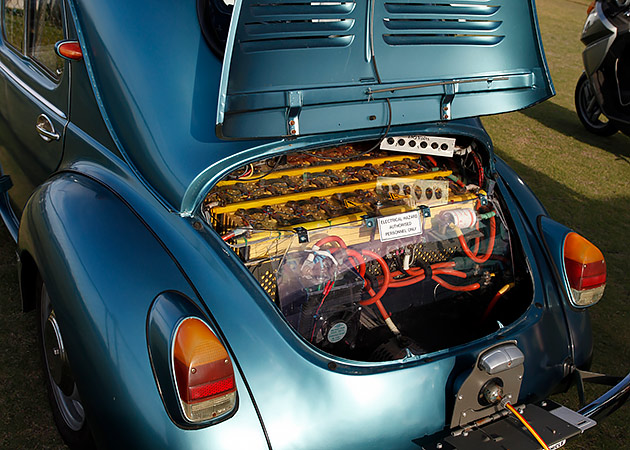 A metallic green-coloured classic car with its boot lid up showing an EV battery pack