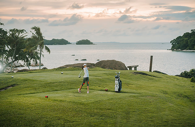 A woman is playing golf on a course with an ocean backdrop