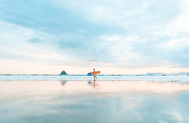 A man walking with a surfboard along a beach