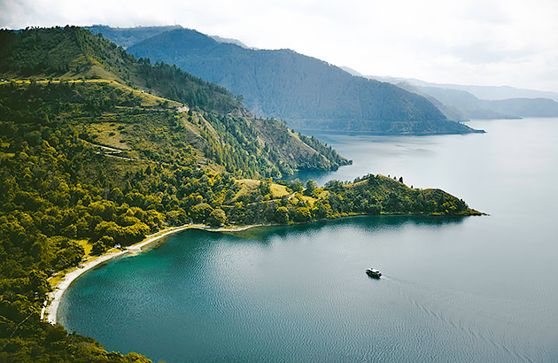 A calm bay surrounded by a tree-covered mountainous landscape