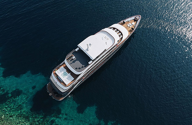 An aerial image of a small luxury cruise ship in clear waters