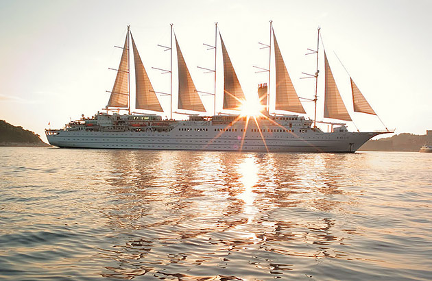 A cruise ship with many sails at sunset seen on the horizon