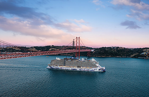 A ship cruising past a bridge at sunset