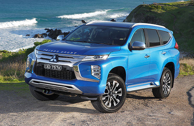 A blue Mitsubishi Pajero Sport parked on a hillside with ocean in the background