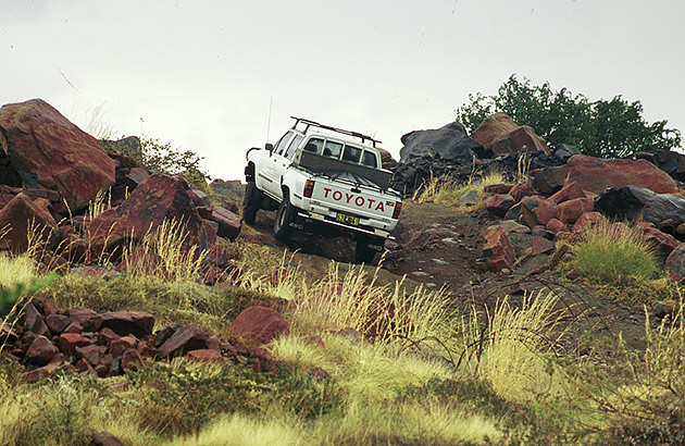 A four-wheel drive ute driving up a hill over rocks