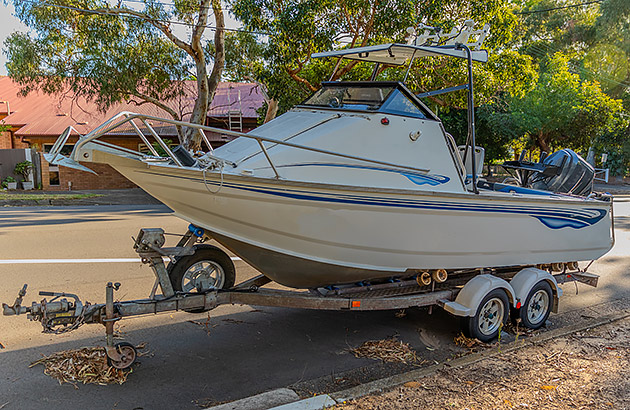 A boat on a trailer parked on the side of a road