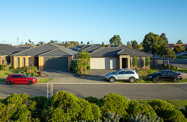 A suburban street with one car parked on the road and two on the verge