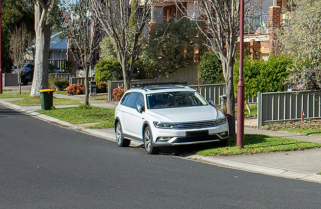 A parked car with its passenger-side tyres on a verge