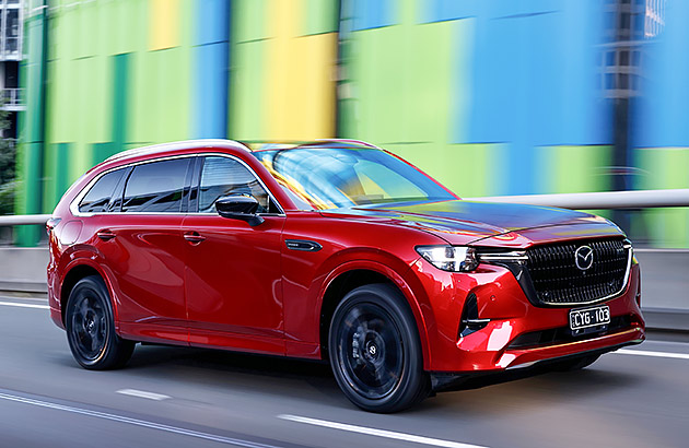 A red Mazda CX-80 driving along a city street