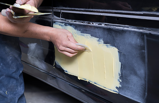 A close up of a person patching rust on the side panel of a car