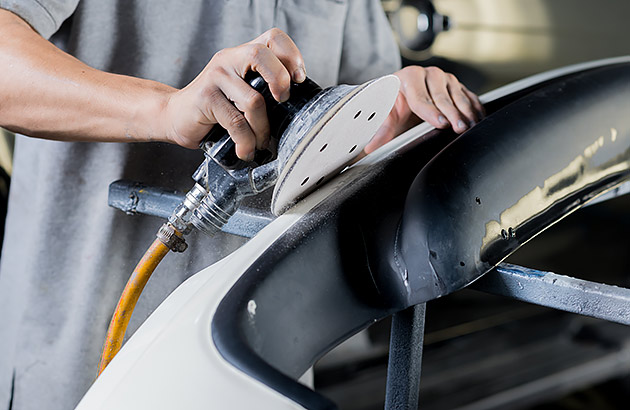 A close up of a person using an electric sander on a car panel