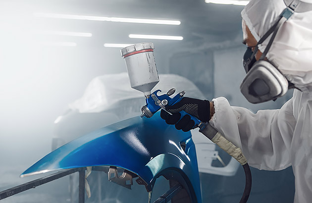 A person spray painting a car wearing full cover overalls and a mask