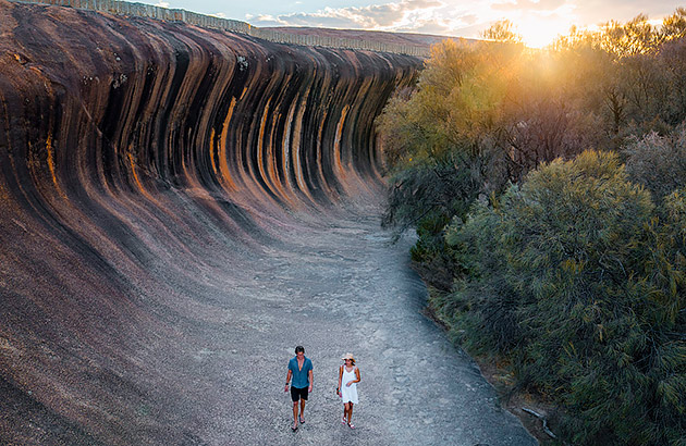 A boat tracks an orca out in the open ocean A man and woman walk along Wave Rock at sunset