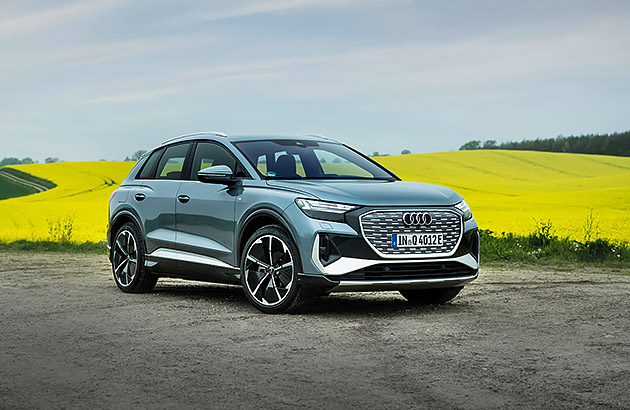 A blue Audi eTron Q4 parked on a rural road near a field of yellow flowers