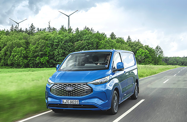 A blue Ford E Transit driving on a rural road